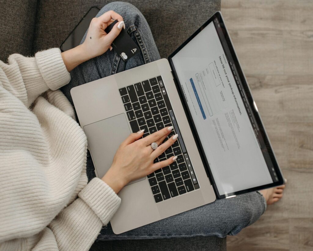 Top view of a woman shopping online using a laptop while sitting on a grey sofa.